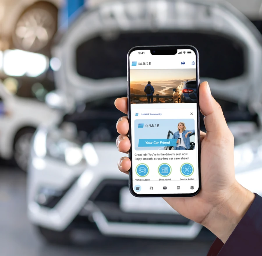 A driver holding their phone with the 1stMILE app open in front of their car