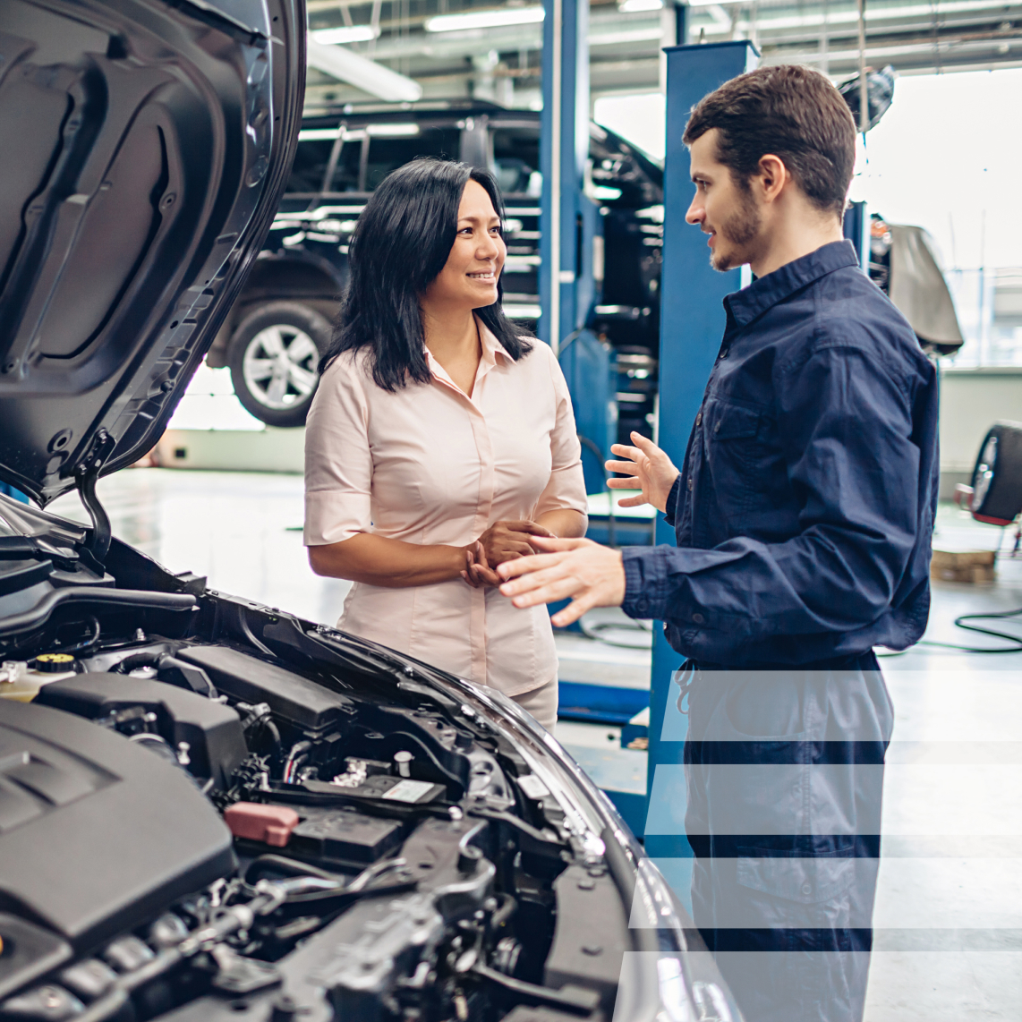 a woman talking to a mechanic next to a vehicle with an open hood